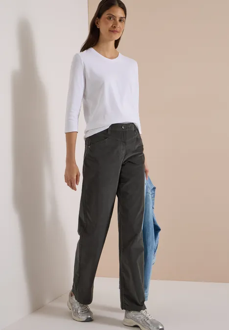High Waist Wide Leg Hose im Loose Fit easy khaki Frau in weißem 3/4-Shirt, schwarzen Jeans und Sneakers hält eine hellblaue Jacke locker in der Hand.