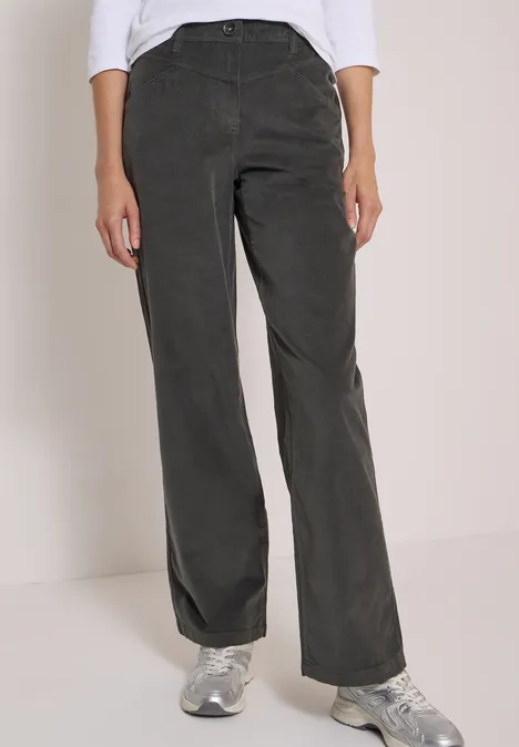 High Waist Wide Leg Hose im Loose Fit easy khaki Frau trägt dunkelgraue Cordhose mit weitem Bein und Sneakers, vor hellem Hintergrund.