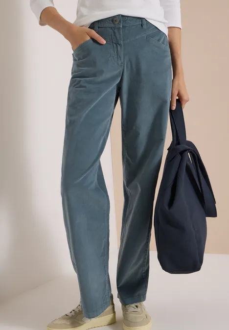 High Waist Wide Leg Hose im Loose Fit dove blue Frau in weiten blauen Cordhosen, weißen Sneakern, weißem Oberteil, hält eine dunkelblaue Tasche.