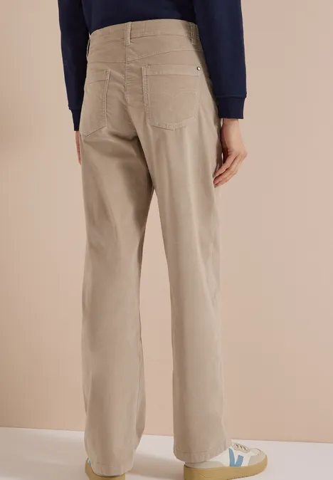 High Waist Wide Leg Hose im Loose Fit silvery beige Person von hinten in beiger, weiter Bundfaltenhose und weißen Sneakers vor neutralem Hintergrund.