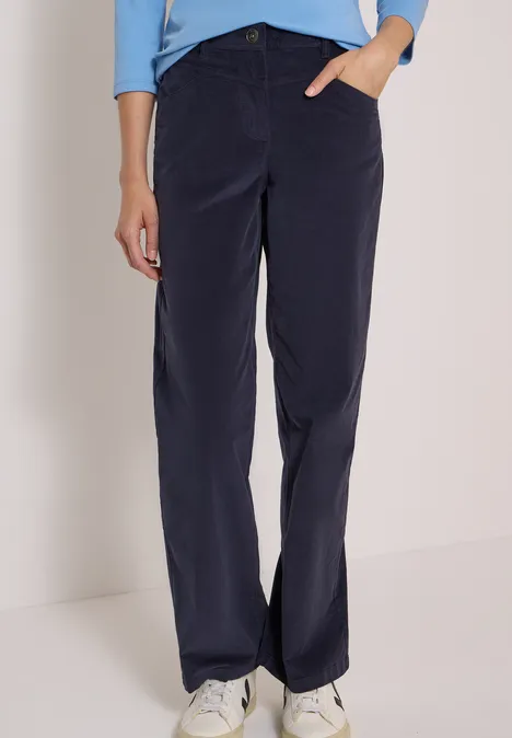 High Waist Wide Leg Hose im Loose Fit dark blue corduroy Person in dunkelblauer Cordhose, hellblauem Shirt und weißen Sneakern vor hellem Hintergrund.