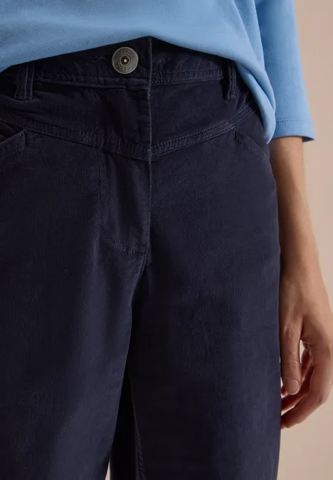 High Waist Wide Leg Hose im Loose Fit dark blue corduroy Ausschnitt einer Person mit dunkelblauer Cordhose und hellblauem Langarmshirt, Hand seitlich sichtbar