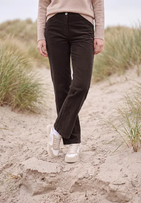 Persoon staat op duinzand, draagt zwarte broek, licht trui en witte sneakers; helmgras op de achtergrond.