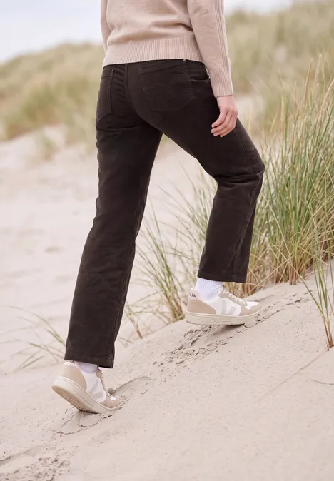 Persoon in zwarte broek en lichte schoenen beklimt een duin met helmgras.