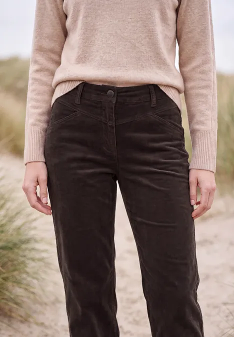 Persoon staat op het strand voor duingras, draagt een beige trui en zwarte corduroybroek
