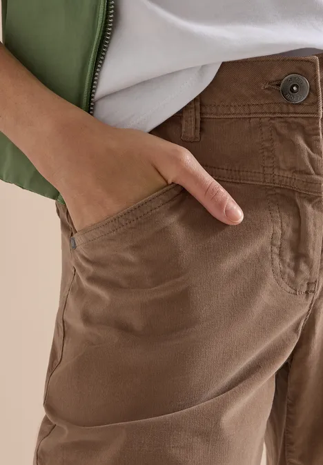 High Waist Wide Leg Hose im Loose Fit earthy taupe Nahaufnahme: Hand in der Tasche einer braunen Hose, dazu grüner Mantel und weißes Shirt.