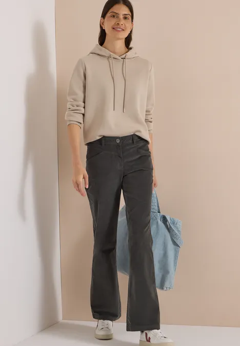 High Waist Bootcut Hose im Slim Fit easy khaki Frau in beigem Hoodie, weiten schwarzen Jeans, hält eine blaue Jeansjacke.