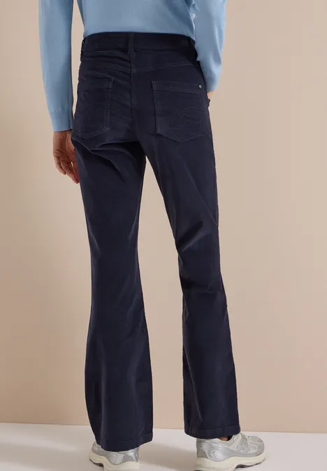 Rückansicht einer Person in hellblauem Langarmshirt und dunkelblauen, ausgestellten Hosen.