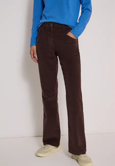 Person trägt braune Cord-Schlaghose, blaues Oberteil und helle Sneaker.
