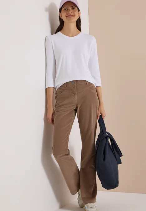 High Waist Bootcut Hose im Slim Fit earthy taupe Eine Frau lehnt an einer Wand, trägt weißes Oberteil, braune Hose, Cap und hält eine dunkelblaue Tasche.