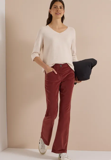 High Waist Bootcut Hose im Slim Fit dark russet red Eine Frau in weißem V-Pullover und roter Hose hält ein dunkelblaues Kleidungsstück.