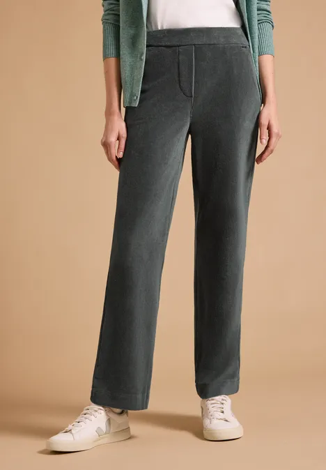 Frau trägt dunkelgraue Cordhose mit geradem Schnitt, Seitentaschen und weißen Sneakers.