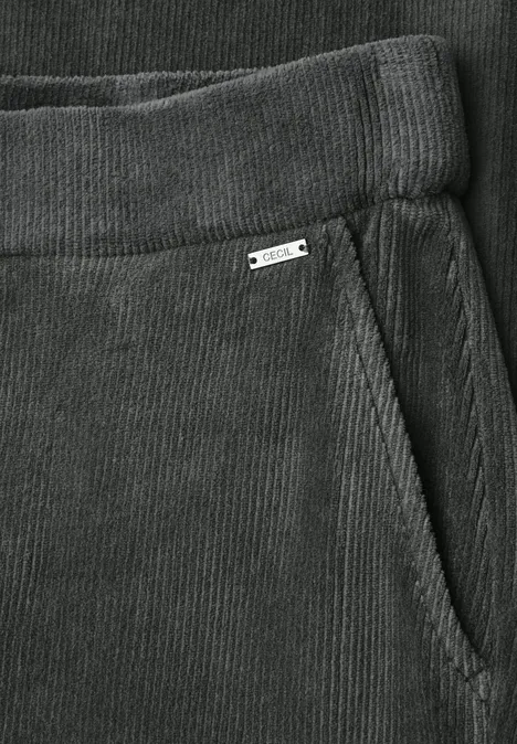 Detailaufnahme einer grauen Cordhose mit elastischem Bund und seitlicher Tasche mit kleinem Metallschild.