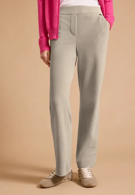 Beige Jogginghose mit seitlichen Taschen und hellen Sneakern vor neutralem Hintergrund.