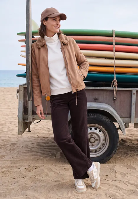 High Waist Straight Leg Hose im Loose Fit berry red Eine junge Frau lehnt am Surfbrett-Anhänger am sandigen Strand, trägt lässige Kleidung und Cap.
