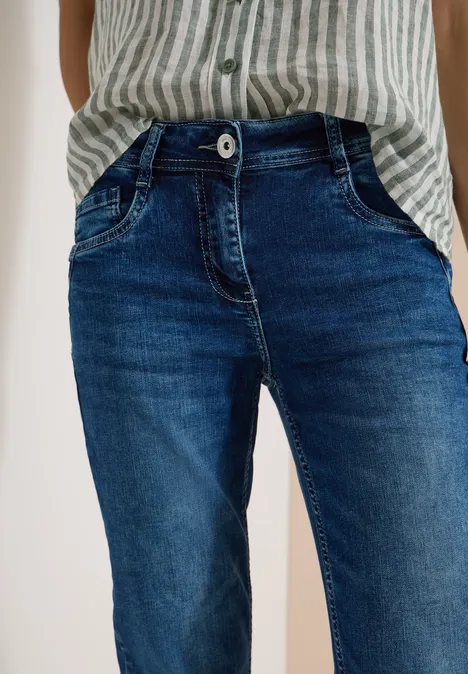 Une personne porte un jean bleu et une chemise rayée, les mains dans les poches.