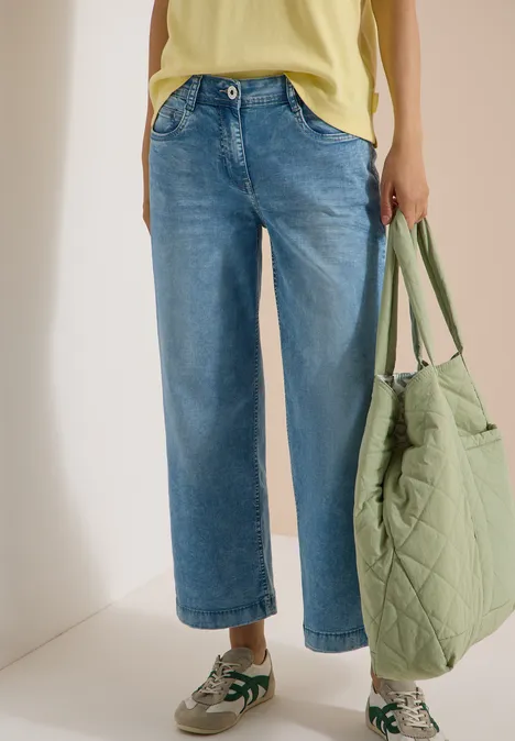 Personne porte un jean large bleu, un haut jaune, un sac matelassé vert et des baskets.