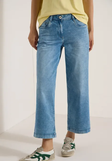 Une personne porte un jean large cropped bleu clair et des baskets sur fond blanc.