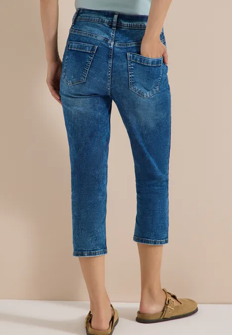 Femme en jean bleu ample mi-mollet avec poches arrière apparentes et ourlet retroussé.