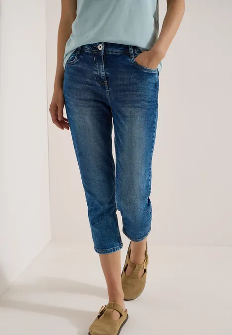 Une personne porte un jean bleu retroussé et des mocassins beiges devant un mur blanc.