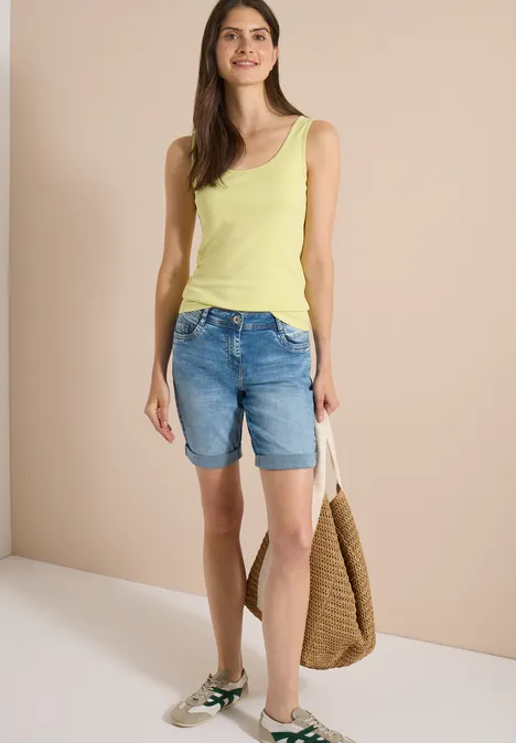 Short taille haute Slim Leg, coupe ajustée authentic used wash Femme portant un débardeur jaune, bermuda en jean, baskets vertes et sac en paille sur fond clair.