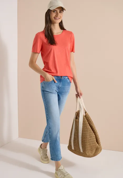 Jean taille mi-haute à coupe Straight Leg et coupe décontractée light blue wash Femme en T-shirt rouge, jean bleu, baskets blanches, portant un sac tressé.