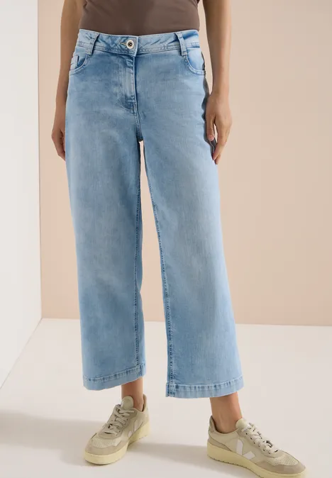 Frau trägt helle, weite 7/8-Jeans und beigefarbene Sneaker.
