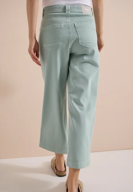 Modell von hinten in pastellgrünen, weiten 7/8-Hosen und flachen Sandalen.