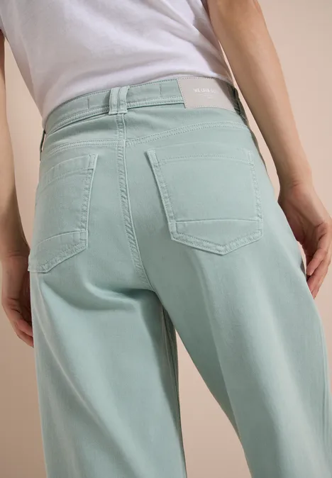 Rückansicht einer Person in helltürkisfarbenen, taillenhohen Jeanshose.