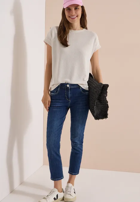 Mid Waist Slim Leg Jeans im Casual Fit mid blue used wash Dame in weißem T-Shirt, blauen Jeans und weißen Sneakern mit schwarzer Flecht-Tasche