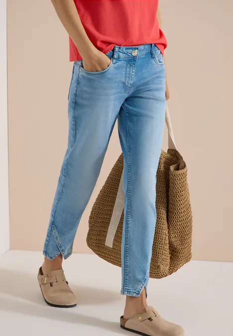Femme en jean bleu clair fendu à la cheville, t-shirt rouge, sac en paille et mocassins beiges.