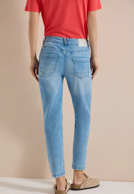 Personne de dos portant un jean bleu clair taille haute, un t-shirt rouge et des mules beiges.