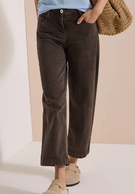 Frau trägt weite dunkelbraune Cordhose mit weißen Slippern und Basttasche.