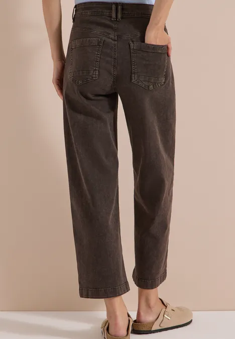 Eine Person trägt weite, dunkelbraune Jeans und beige Halbschuhe, Hände in den Gesäßtaschen.