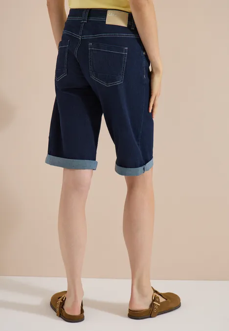 Shorts met High Waist en Wide Leg pijpen in een Loose Fit pasvorm rinsed wash Vrouw van achteren in een donker gewassen omgeslagen denim Bermuda-short met bruine loafers.