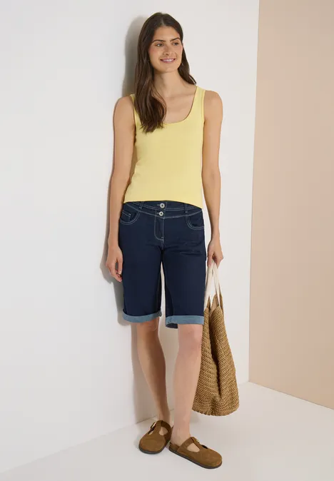 Shorts met High Waist en Wide Leg pijpen in een Loose Fit pasvorm rinsed wash Vrouw in gele top, spijkerbroek bermuda, bruine sandalen en strooien tas voor lichte achtergrond.