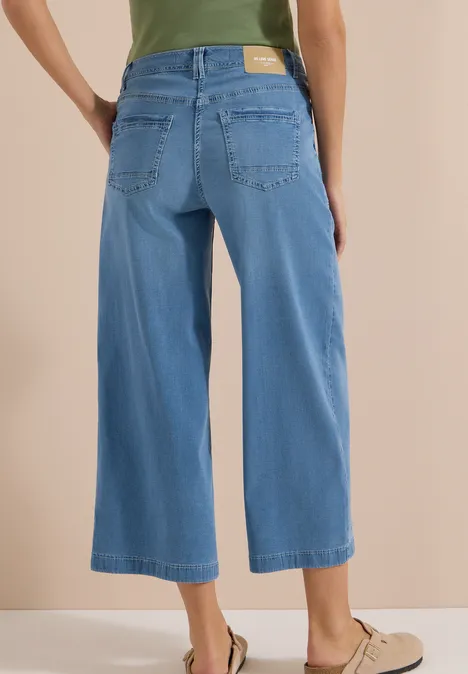 Vrouw van achteren in lichtblauwe, enkellange wijde jeans-culotte met hoge taille en beige instappers.