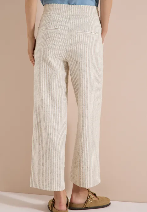 Wide Leg Hose in Seersucker-Qualität grain beige Rückenansicht einer Person in weiß-beigen Nadelstreifenhosen und braunen Loafers.