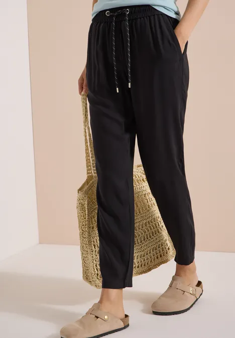 Zwarte, casual broek met koord, gevlochten stroentas en beige instappers.