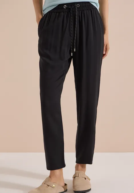 Zwarte, losvallende broek met taillekoord, gecombineerd met beige instappers.