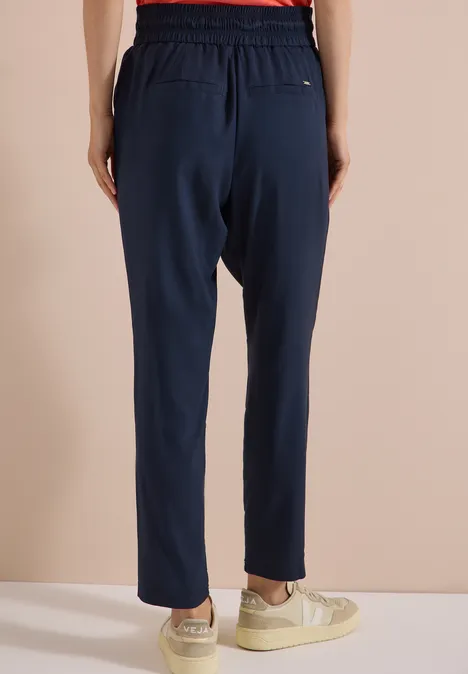Pantalon Mid Waist Slim Leg en coupe loose universal blue Vue arrière d'une personne portant un pantalon de jogging bleu marine, taille élastique, et baskets blanches devant un mur clair