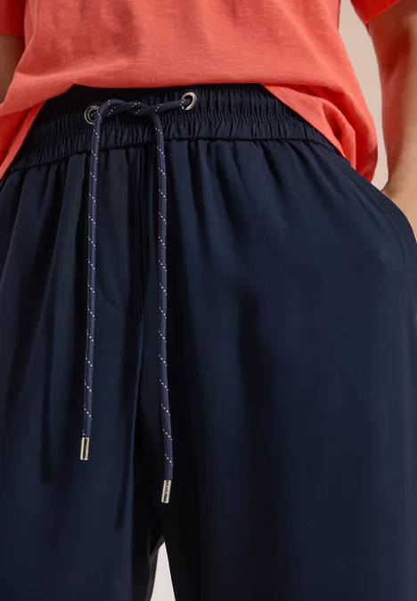 Pantalon Mid Waist Slim Leg en coupe loose universal blue Plan rapproché d'un pantalon bleu marine à cordon de serrage porté avec un haut rouge.