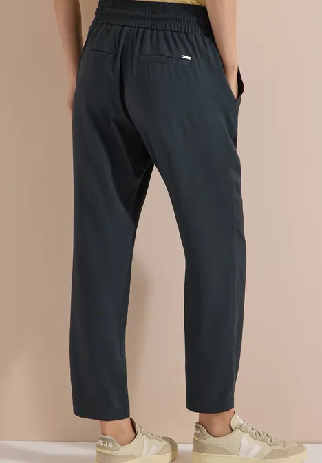 Pantalon noir ample à taille élastique et poches, associé à des baskets claires.
