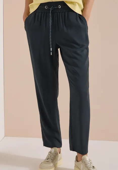 Pantalon décontracté noir à cordon de serrage, porté avec des baskets beige sur fond clair.