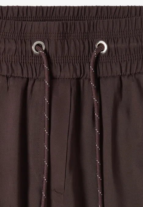 Close-up van een bruine broekband met elastische taille en reflecterende trekkoorden.