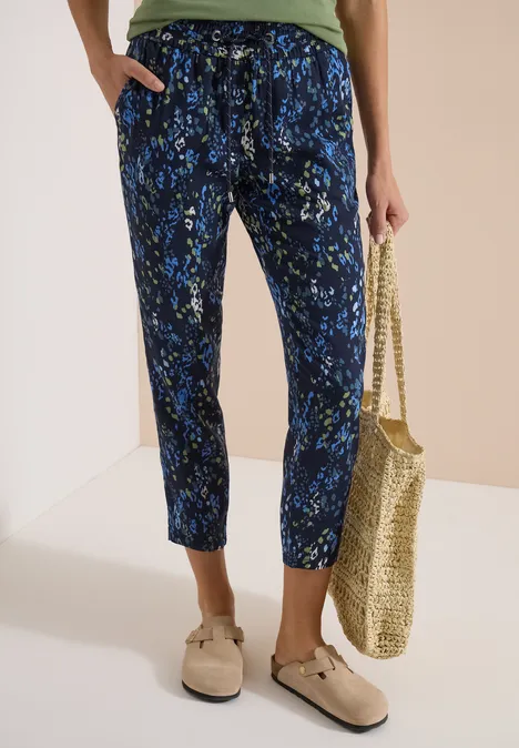 Pantalon fluide bleu marine à fleurs jaunes et blanches, taille élastiquée, sac en paille et mocassins beiges.