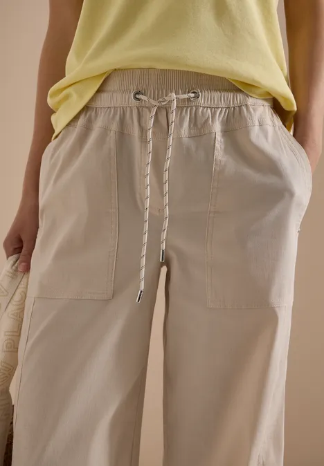 Wijd gesneden lichtbeige broek met elastische taille, koord en opgestikte zakken, gecombineerd met een geel topje.