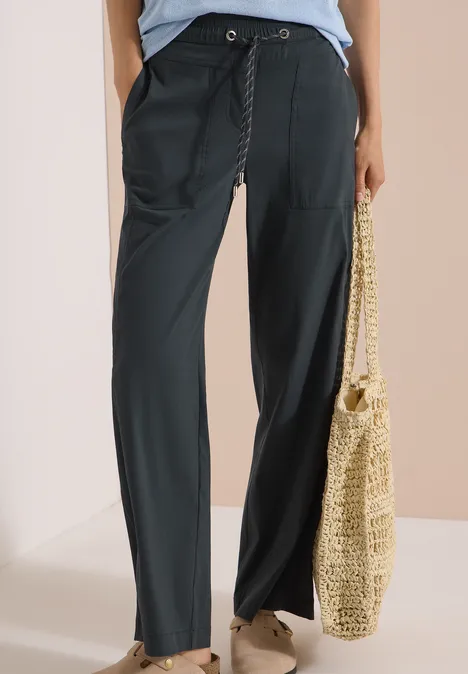 Zwarte comfortabele broek met aantrekkoord, wijde pijpen, gecombineerd met een stro tas.