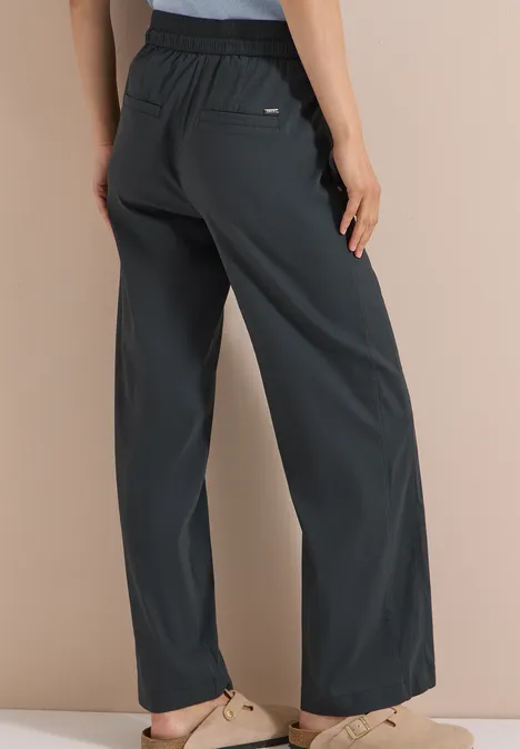 Achteraanzicht van een persoon in wijde donkergrijze broek en beige sandalen.