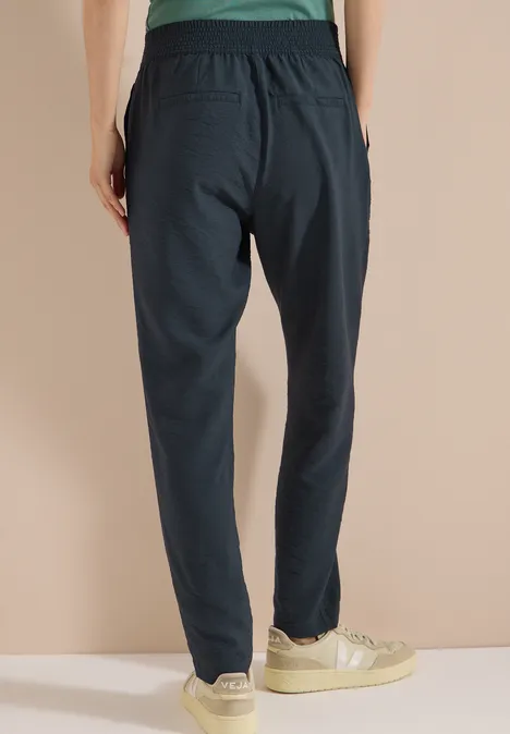 Dunkelblaue Jogginghose von hinten, elastischer Bund, leicht schmal zulaufend, mit Taschen, getragen mit hellen Sneakern.